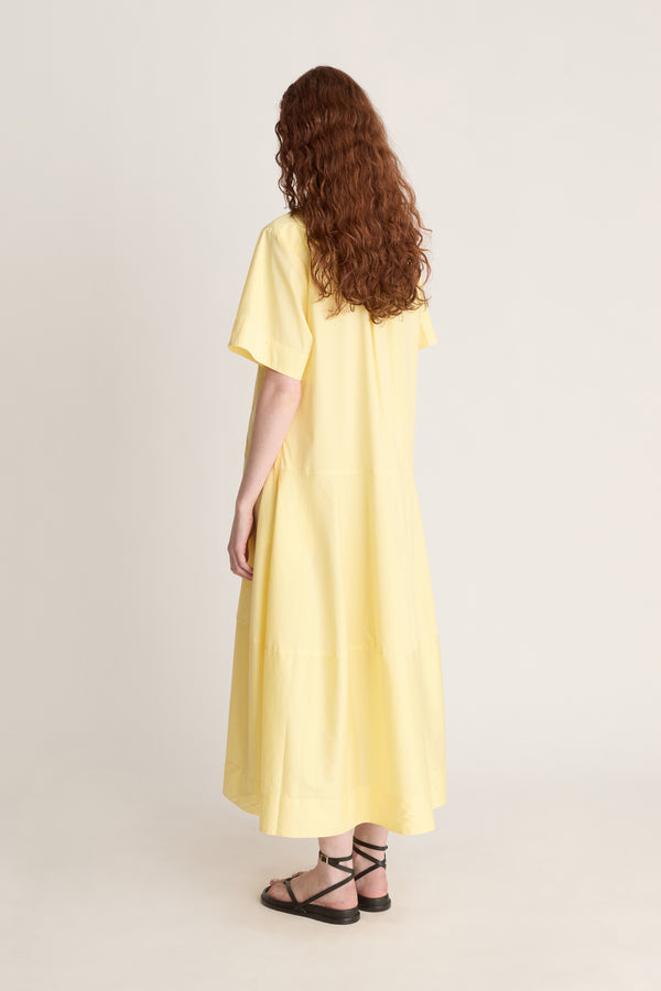Woman wearing a yellow shirt dress against a plain background