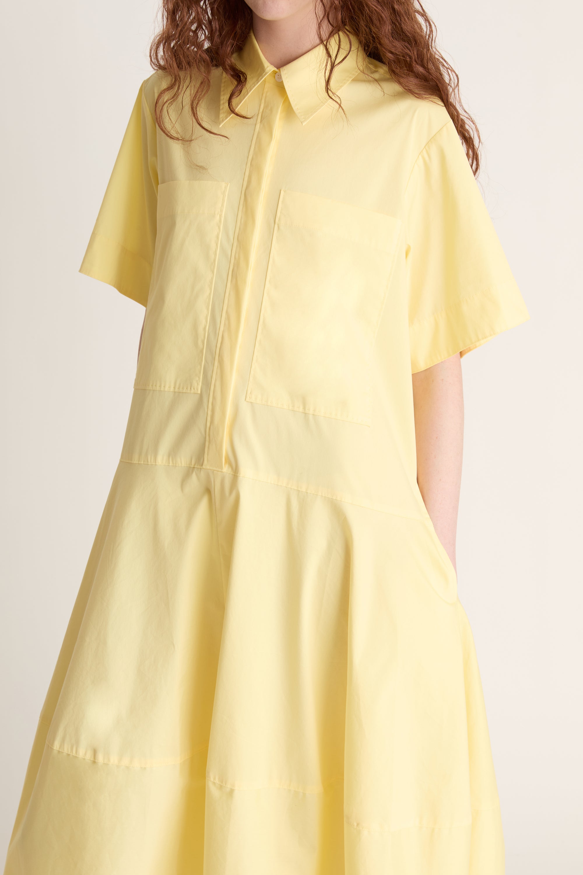 Woman wearing a yellow shirt dress against a plain background