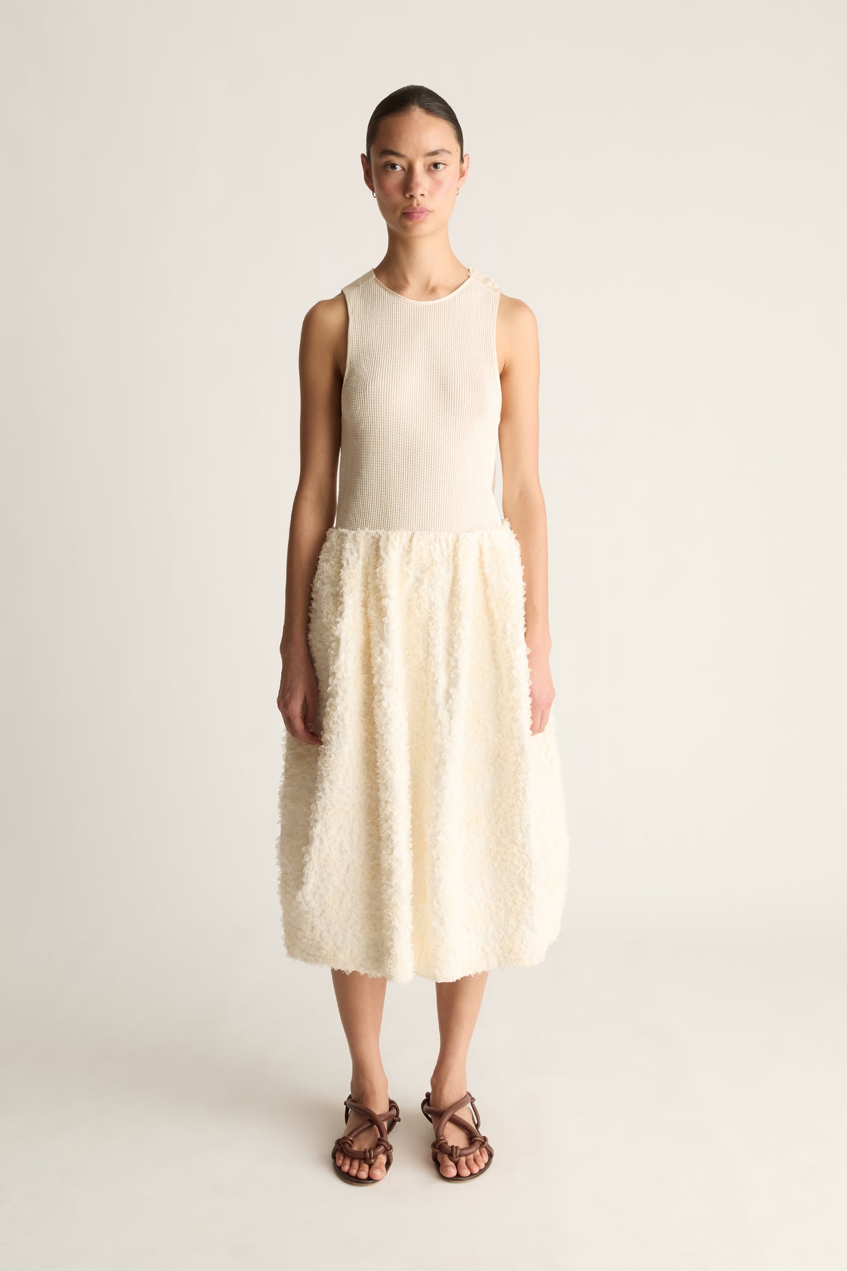 Front view of a woman wearing a cream sleeveless top and cream textured cocoon midi skirt against a white studio background
