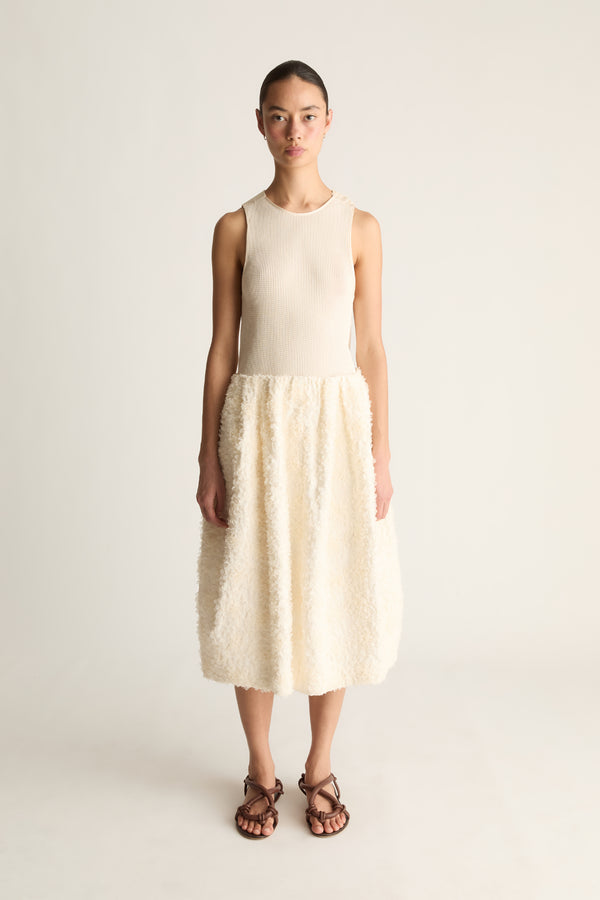 Front view of a woman wearing a cream sleeveless top and cream textured cocoon midi skirt against a white studio background