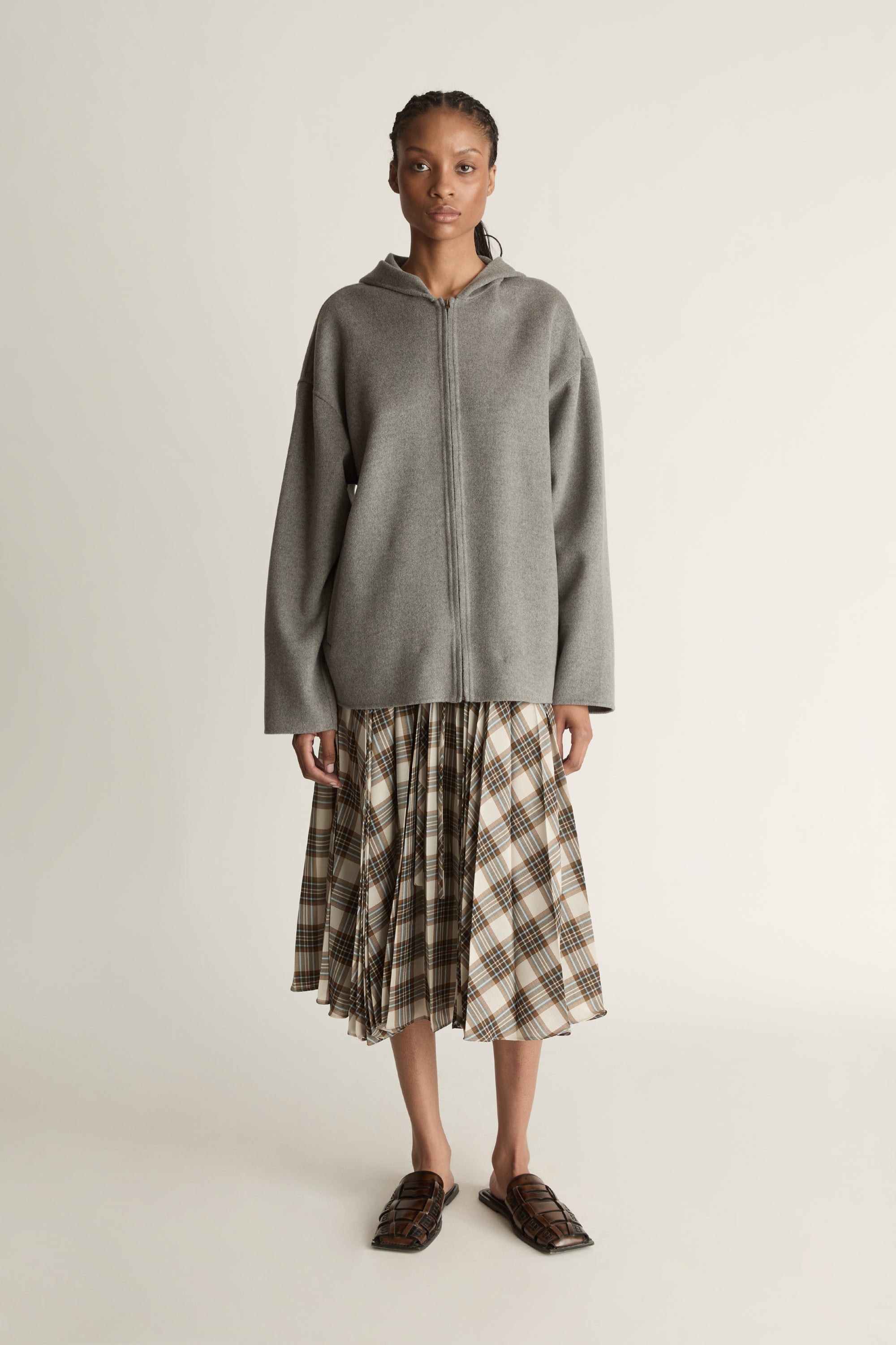 Person wearing a gray hoodie and plaid skirt on a plain background