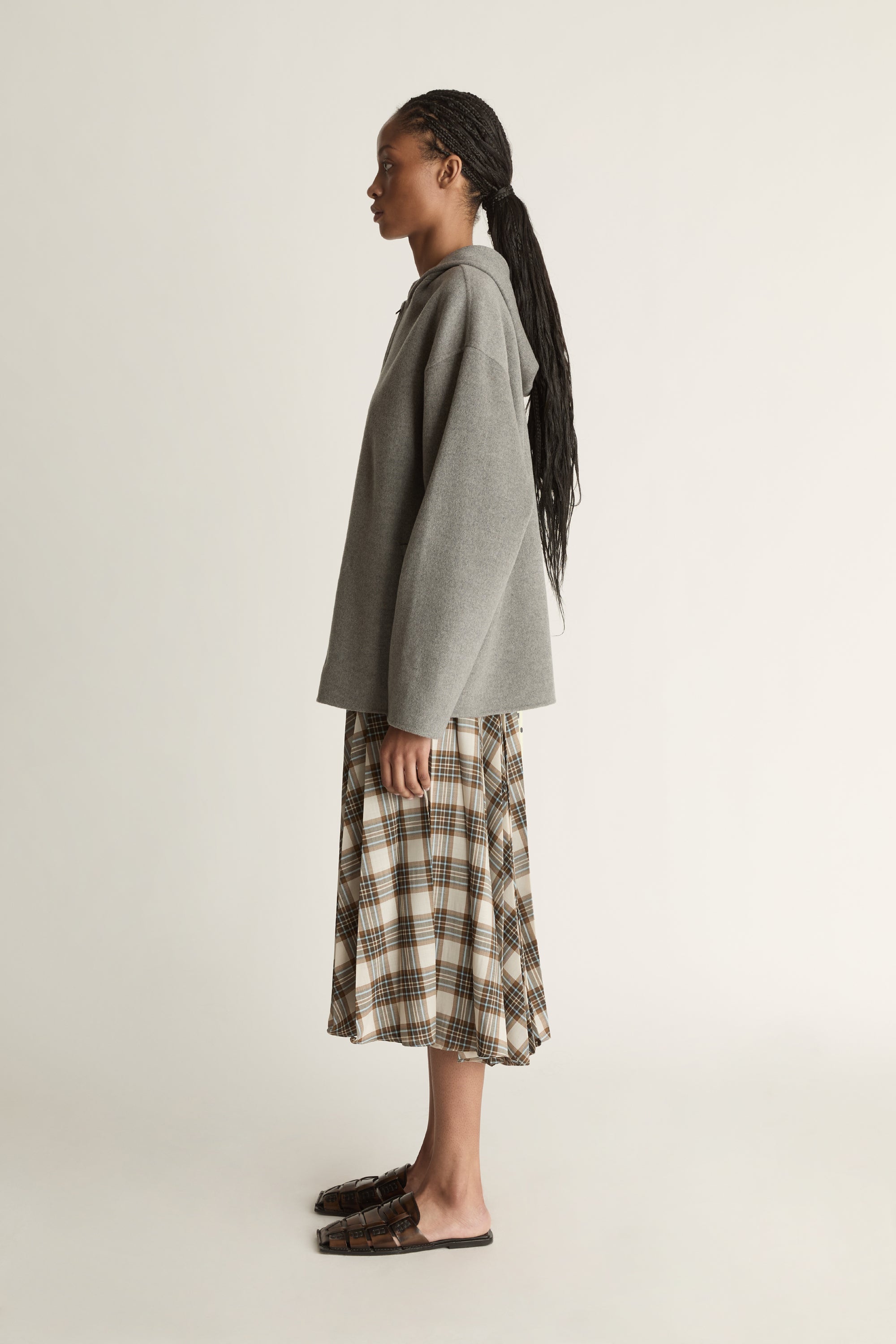 Person wearing a gray hoodie and plaid skirt on a plain background