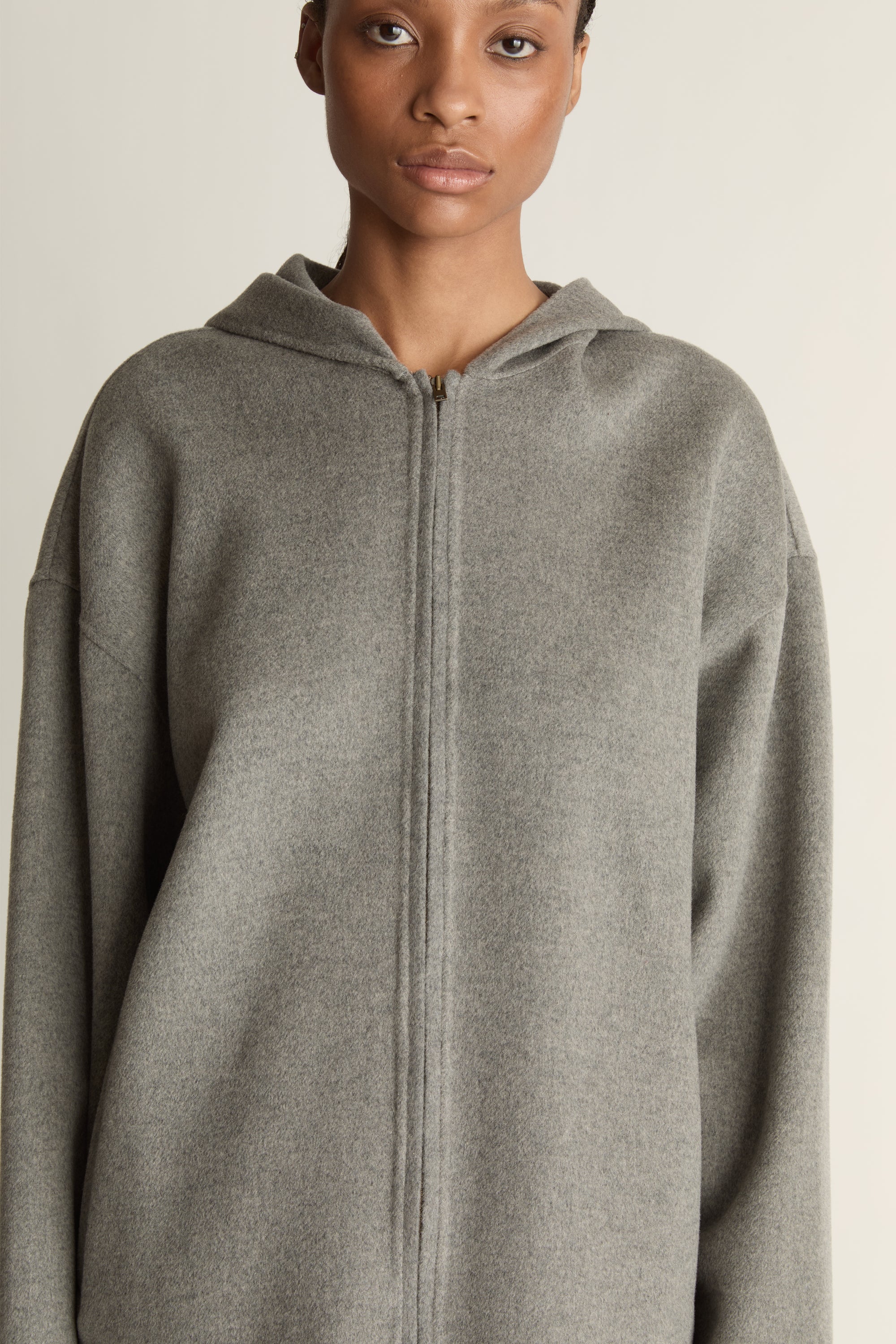 Person wearing a gray hoodie and plaid skirt on a plain background