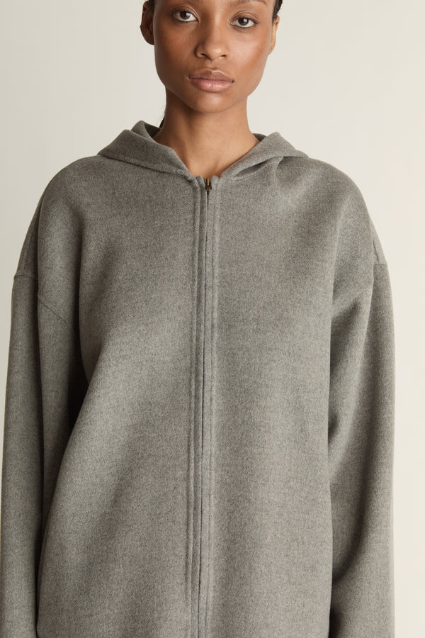 Person wearing a gray hoodie and plaid skirt on a plain background