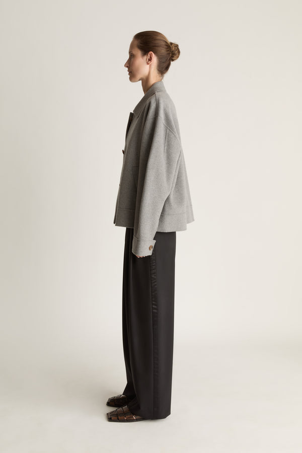 Person wearing a gray jacket and black pants on a white background