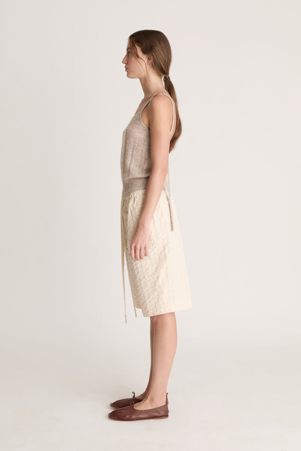 Woman wearing a beige knit cami top and cream coloured shorts on a white background