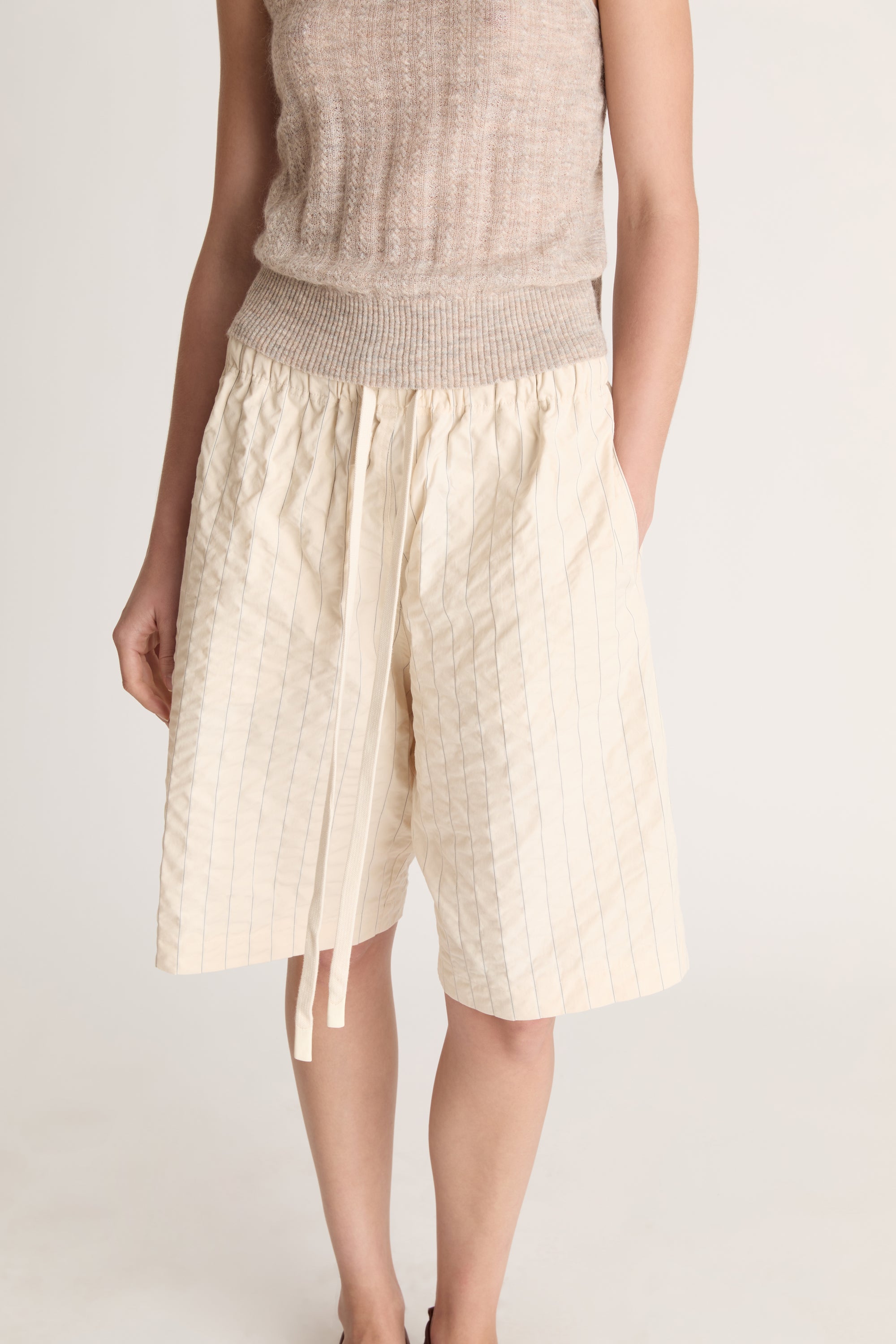 Woman wearing a beige knit cami top and cream coloured shorts on a white background