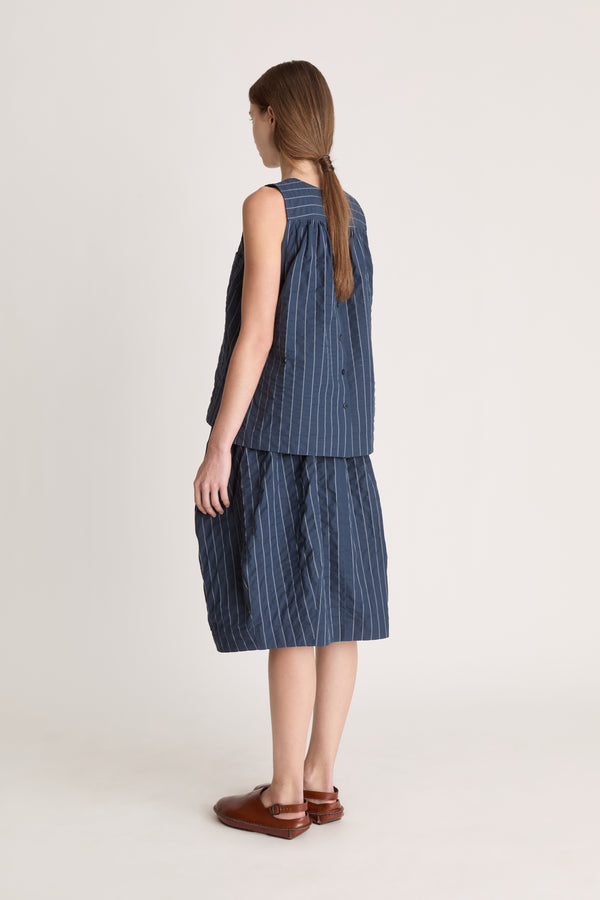 A woman wearing a blue striped top and skirt on a white background