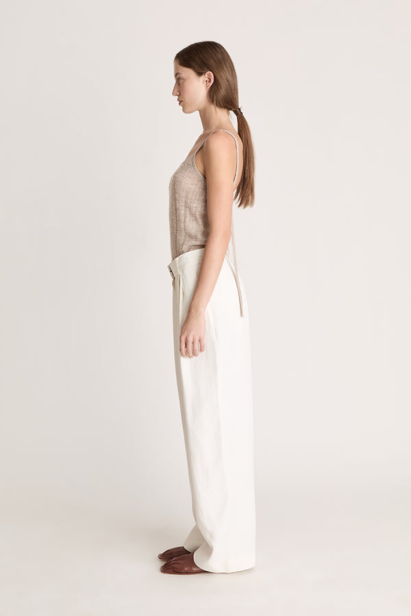 Woman wearing a beige top and white pants on a light background
