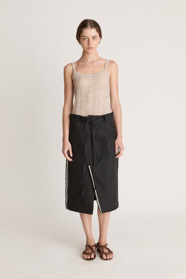 Woman wearing a beige tank top and black wrap skirt on a white background