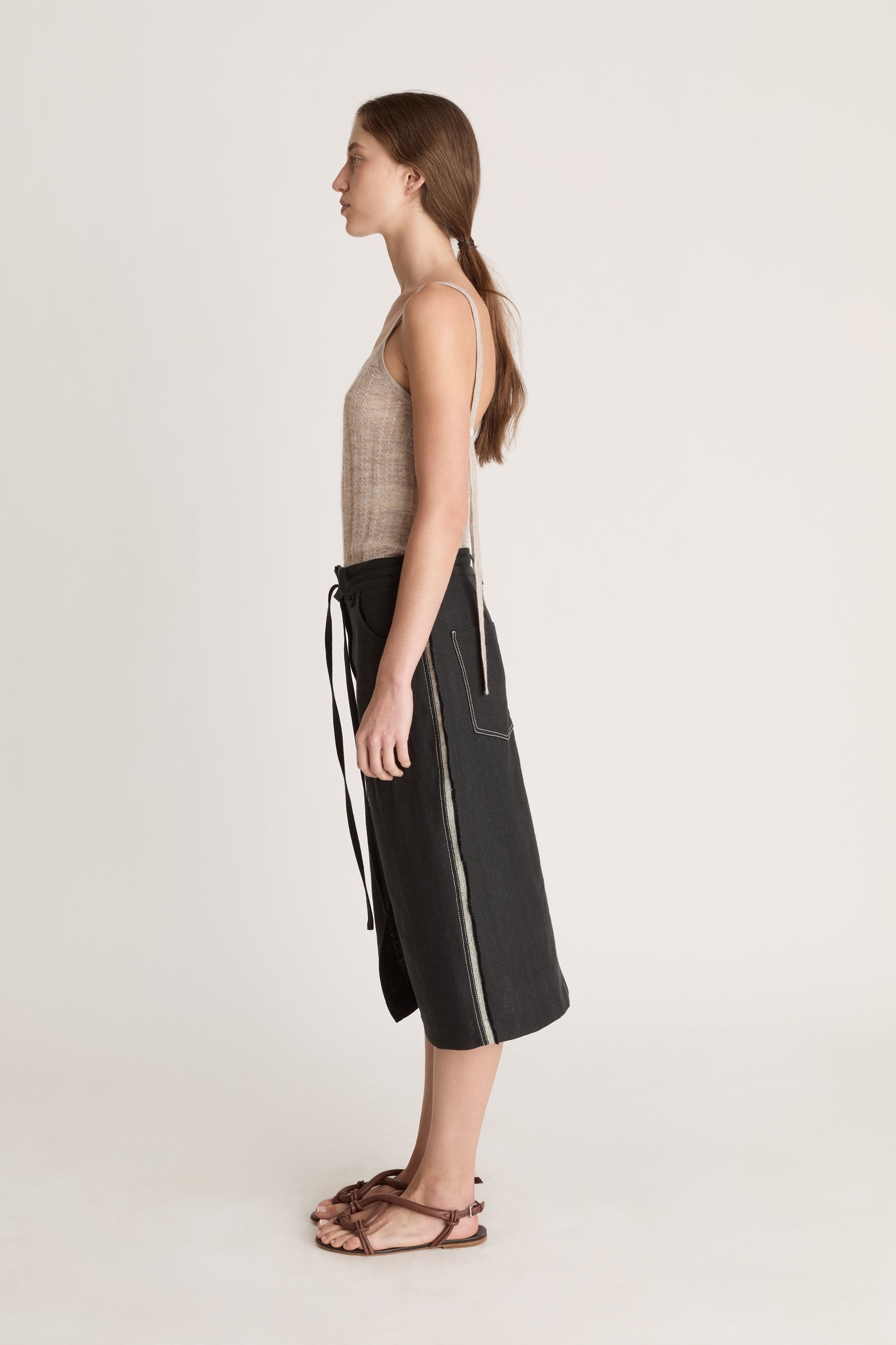 Woman wearing a beige tank top and black wrap skirt on a white background