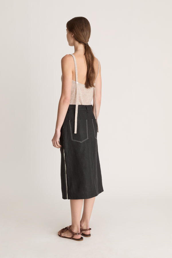 Woman wearing a beige tank top and black wrap skirt on a white background