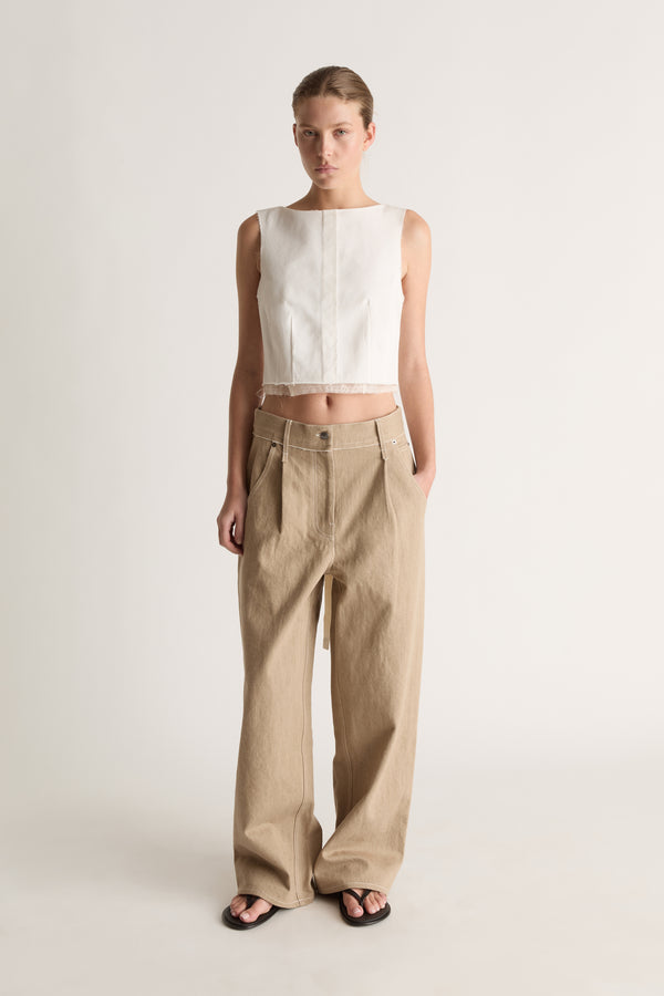 Front view of a woman with hair pulled back in a white panelled crop top, loose beige trousers and black flat sandals