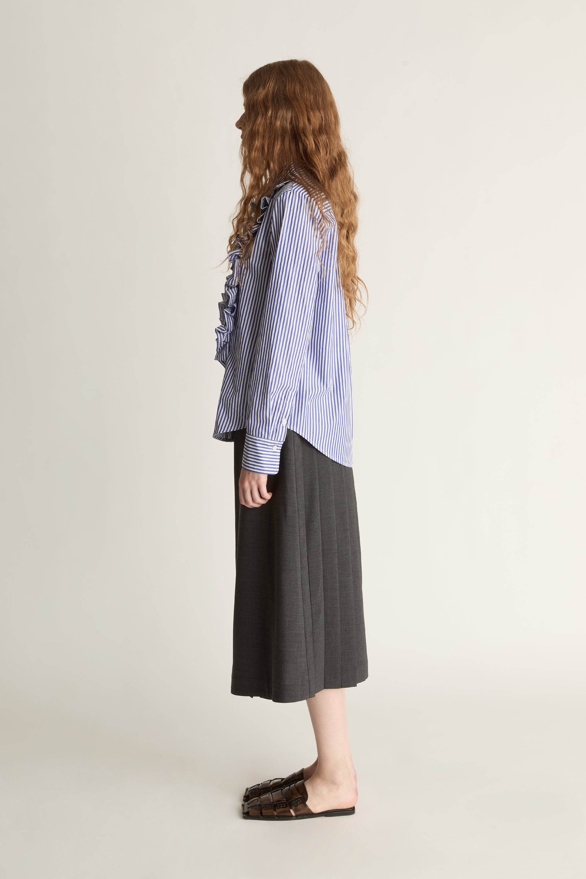 Woman wearing a blue striped shirt with ruffles and a gray skirt on a white background