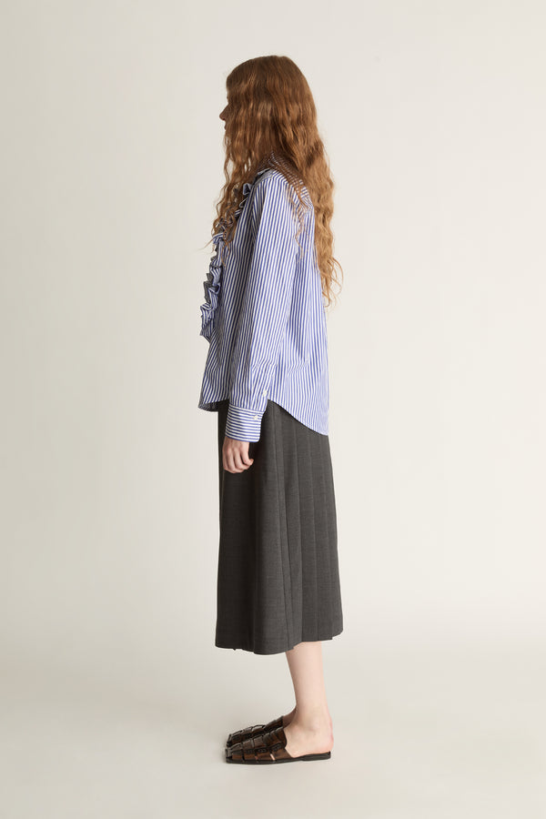 Woman wearing a blue striped shirt with ruffles and a gray skirt on a white background