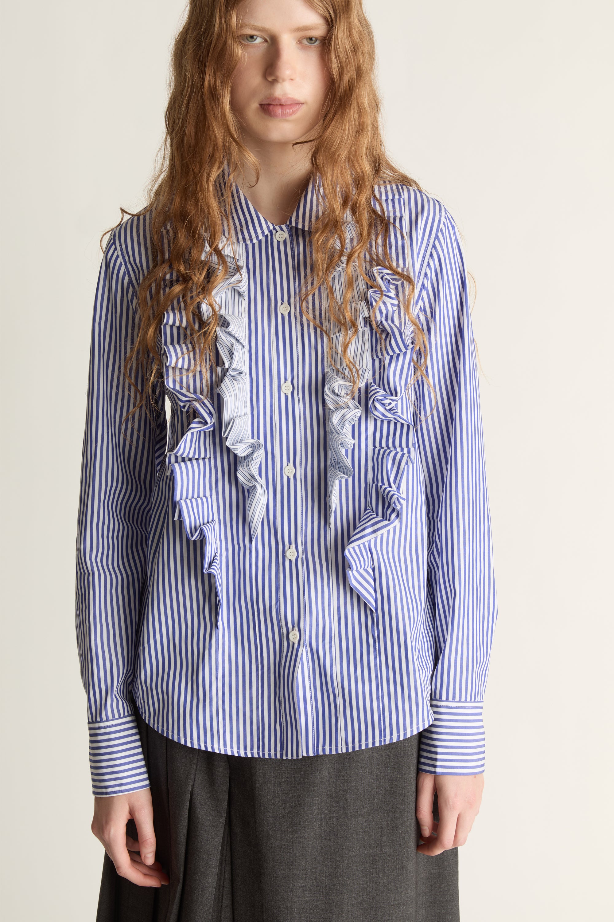 Woman wearing a blue striped shirt with ruffles and a gray skirt on a white background
