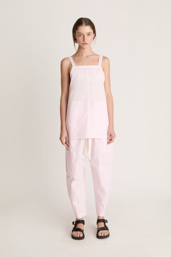 Woman wearing a light pink cami top and light pink pants on a white background