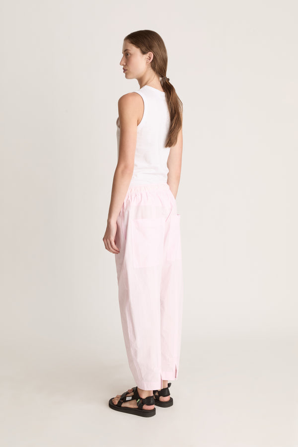 Woman wearing a white sleeveless top and light pink pants on a white background