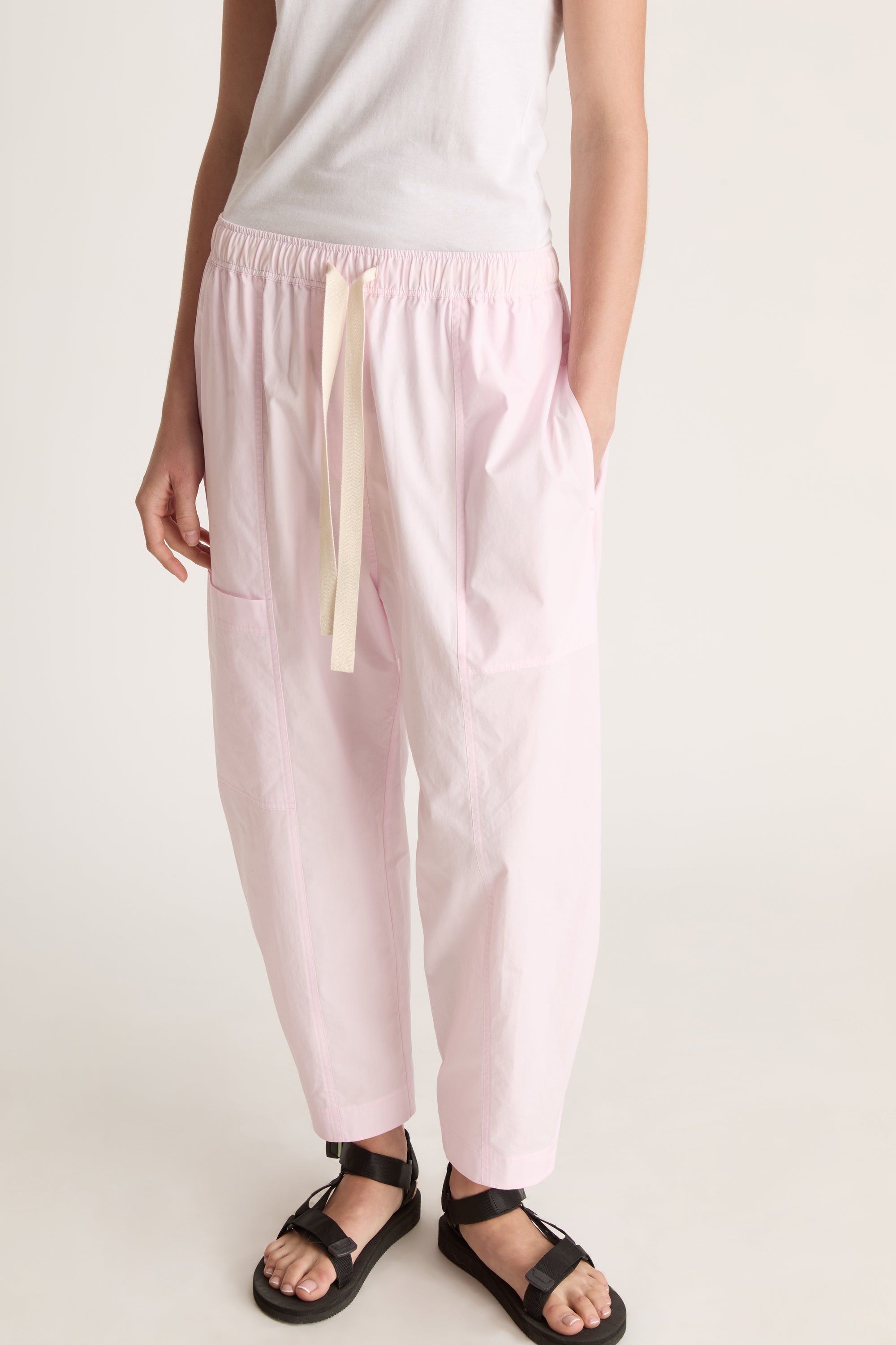 Woman wearing a white sleeveless top and light pink pants on a white background