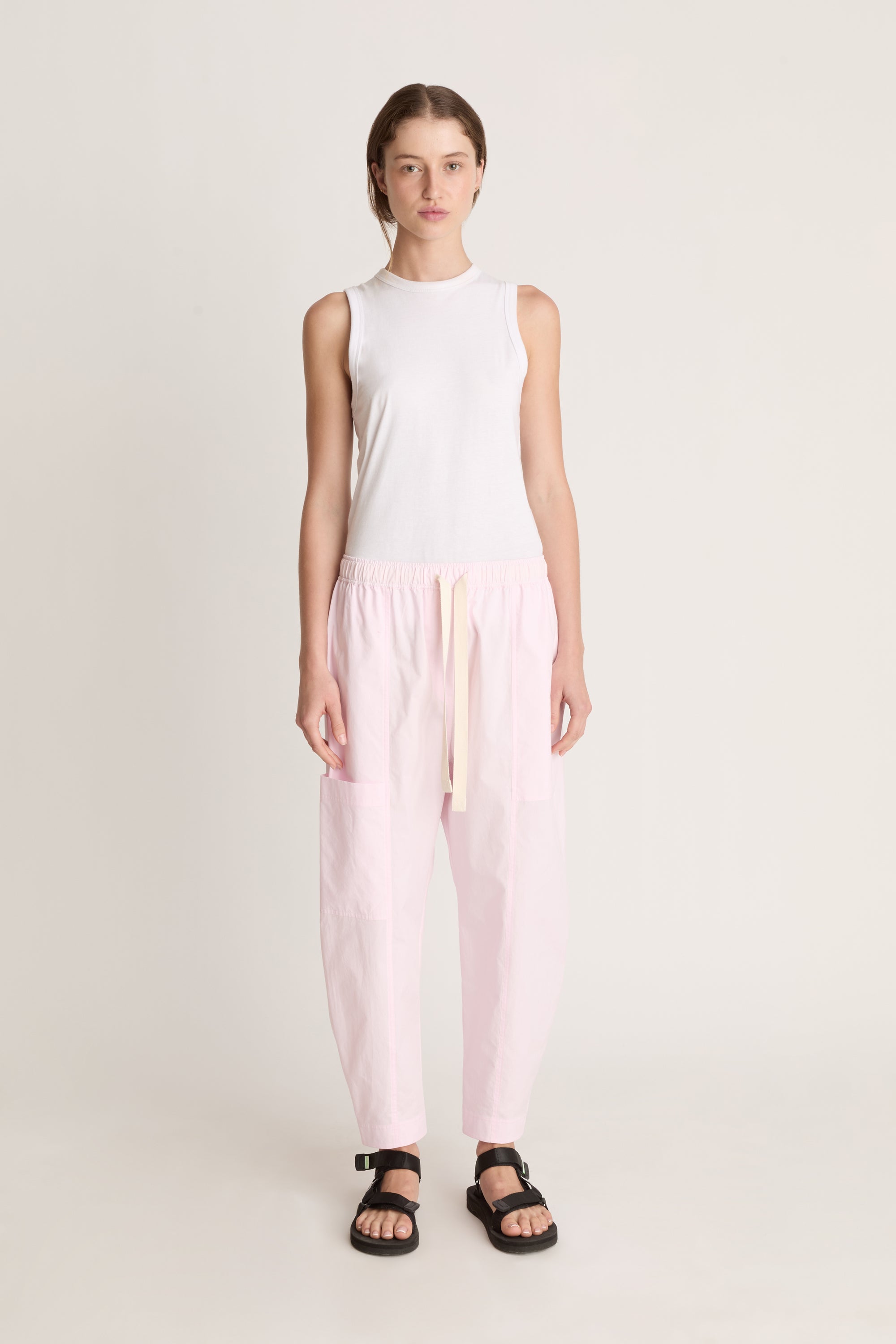Woman wearing a white sleeveless top and light pink pants on a white background