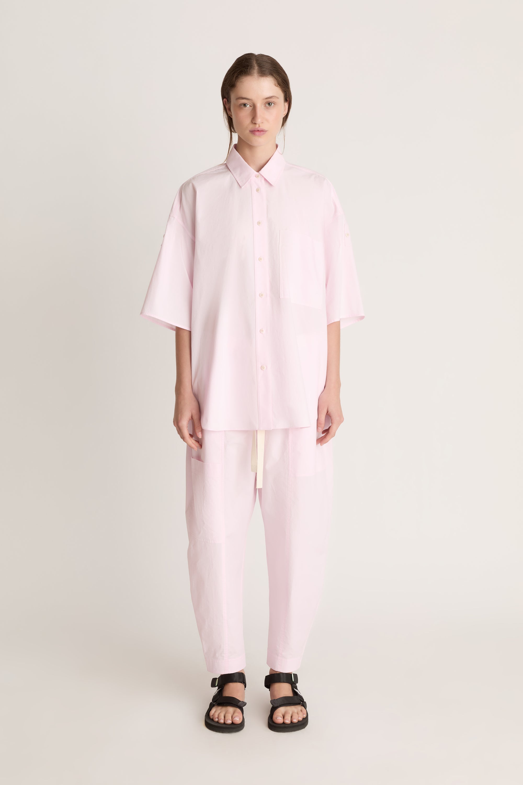 Person wearing a light pink shirt and pants on a white background