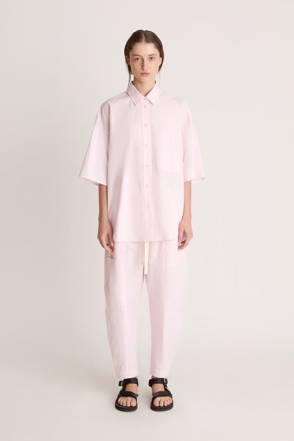 Person wearing a light pink shirt and pants on a white background