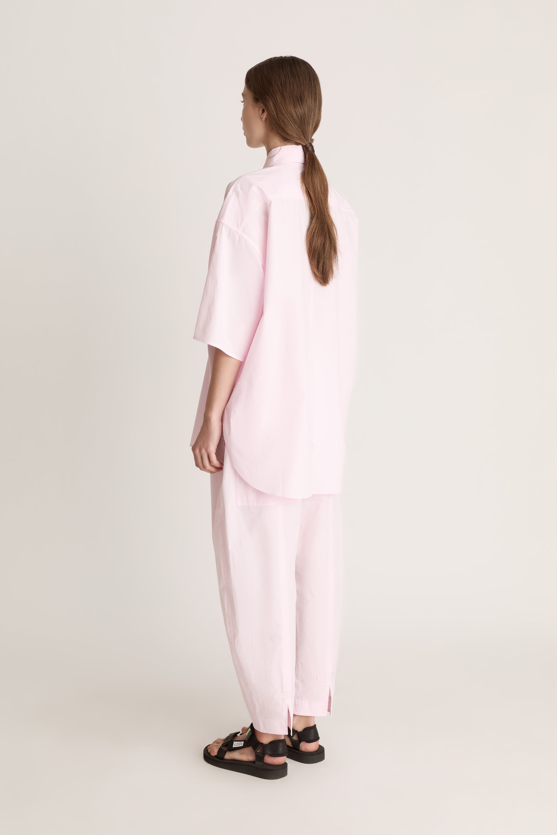 Person wearing a light pink shirt and pants on a white background