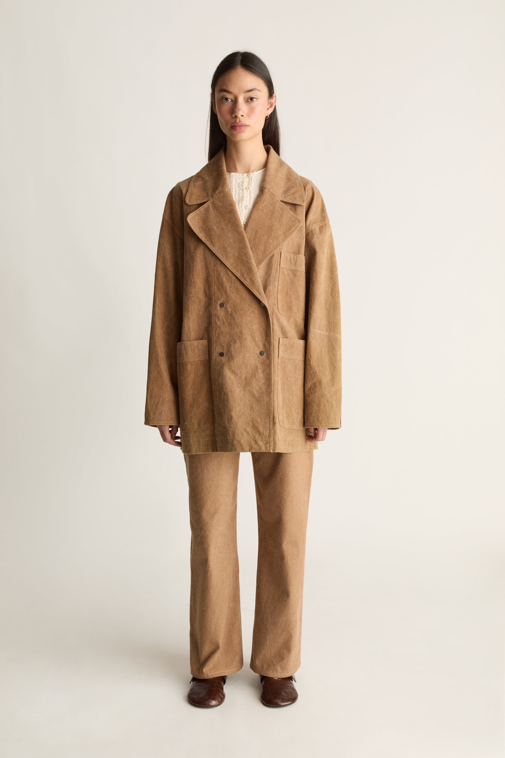 Woman wearing a brown coat and pants on a white background, facing the front.