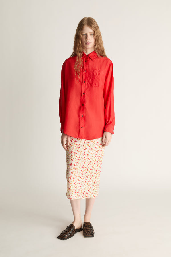 Person wearing a red shirt and patterned skirt on a plain background