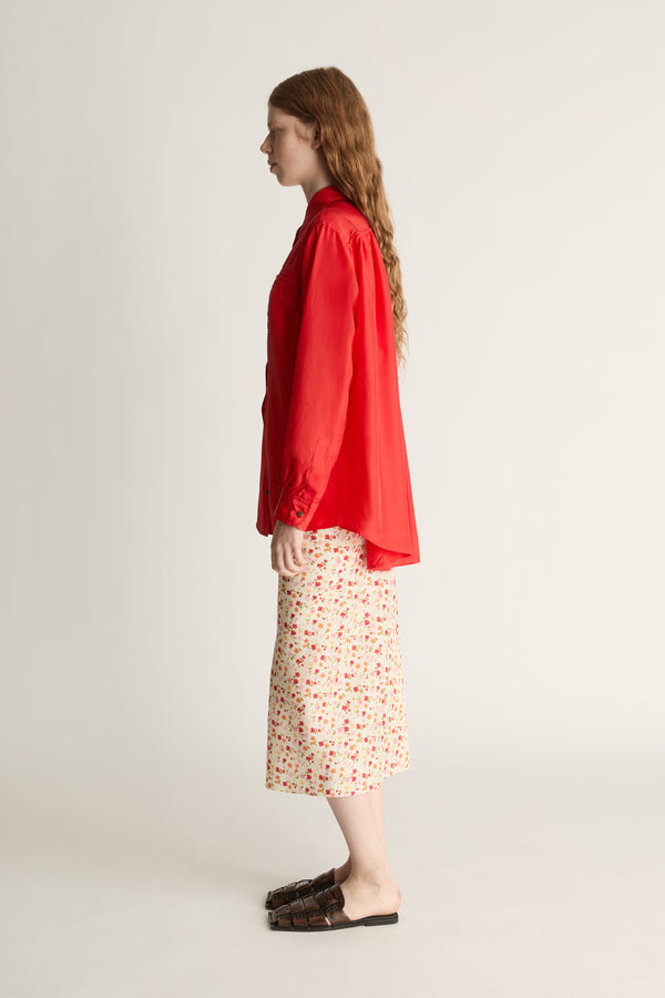 Person wearing a red shirt and patterned skirt on a plain background