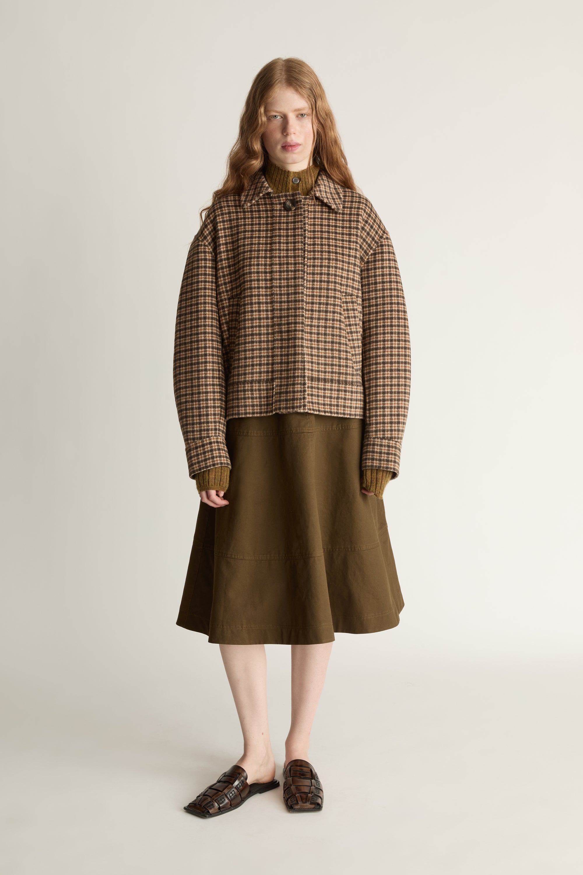 Woman wearing a plaid jacket and brown skirt on a white background