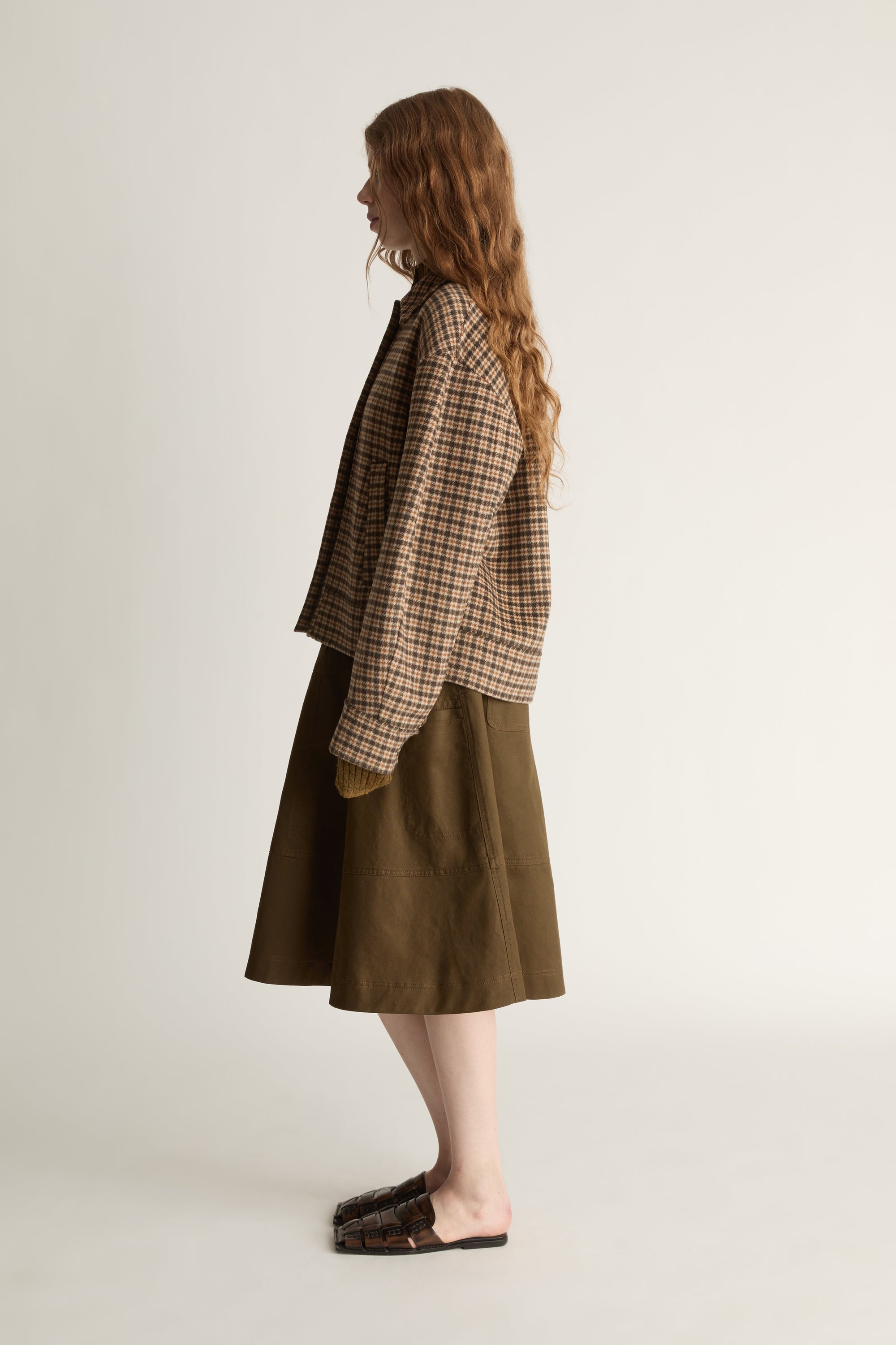 Woman wearing a plaid jacket and brown skirt on a white background