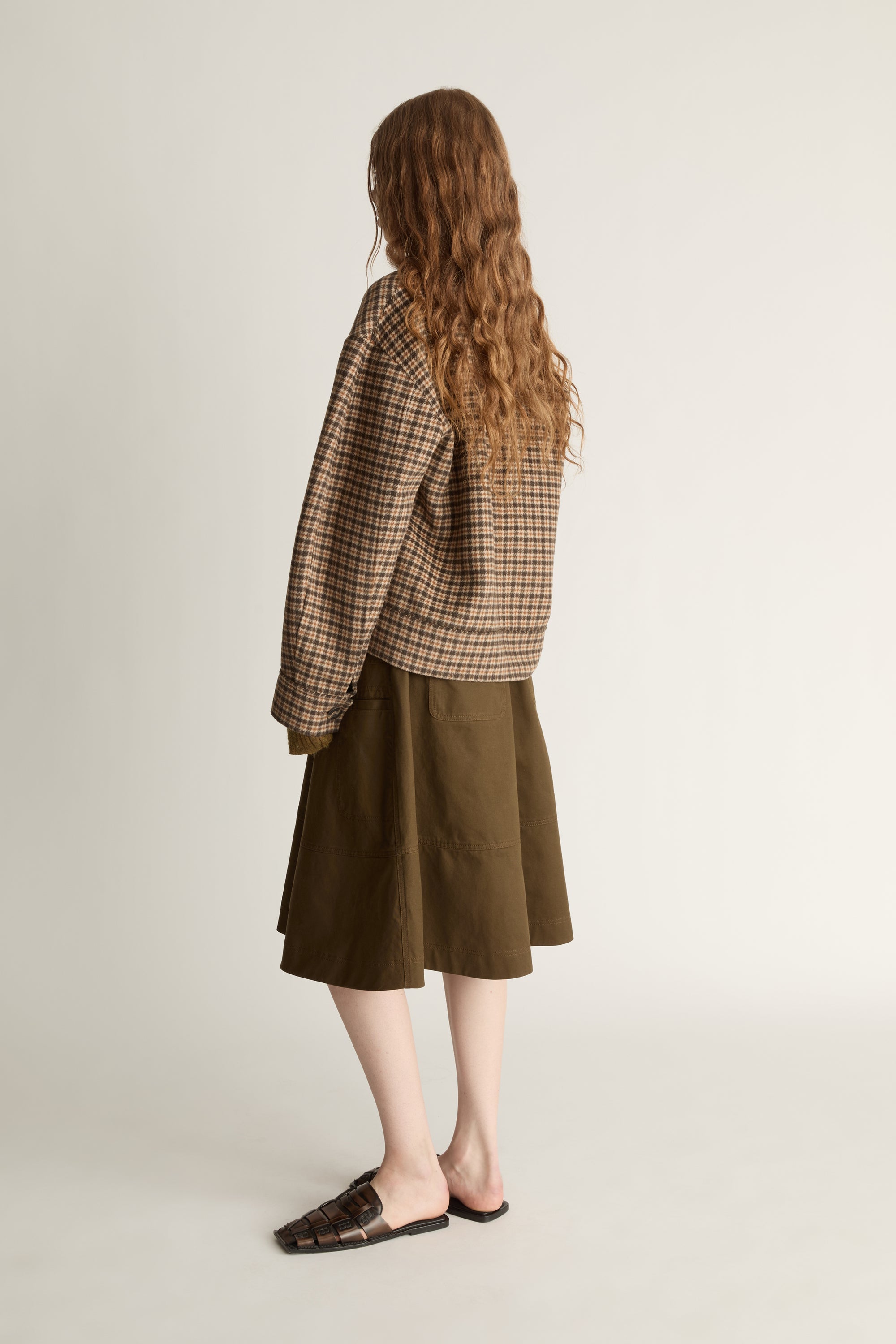 Woman wearing a plaid jacket and brown skirt on a white background