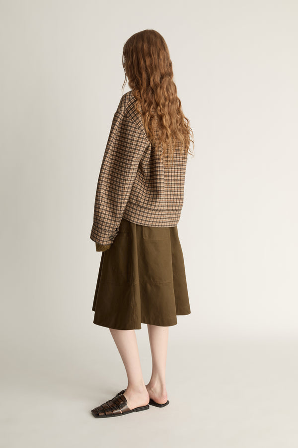 Woman wearing a plaid jacket and brown skirt on a white background