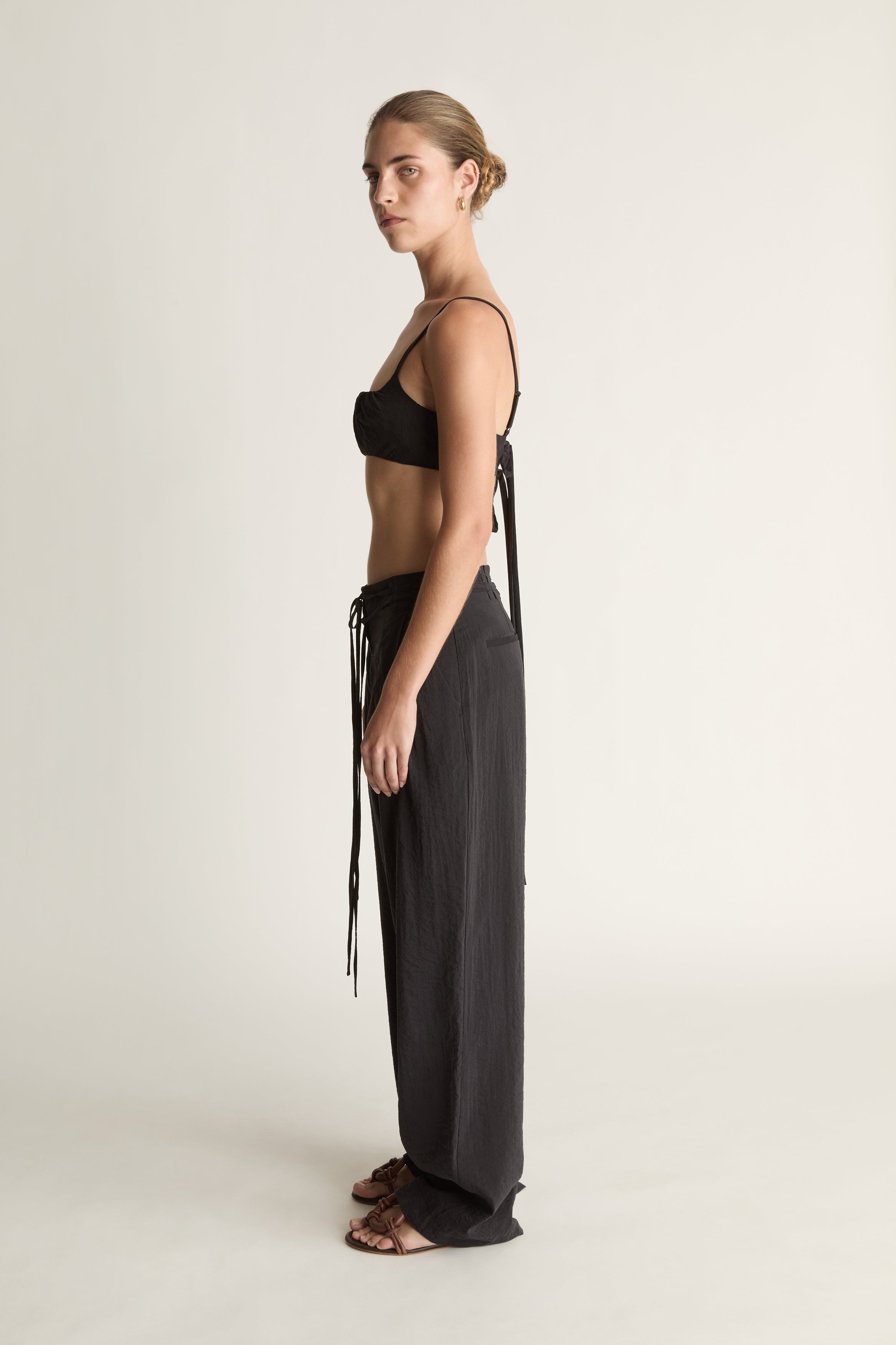 Woman wearing a cropped black top and wide-leg pants on a plain background