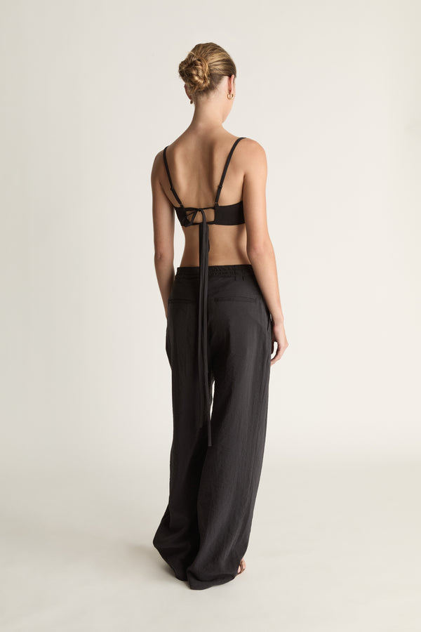 Woman wearing a cropped black top and wide-leg pants on a plain background