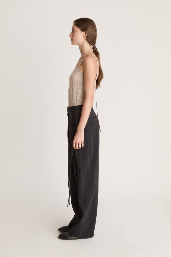 Woman wearing a beige tank top and black pants on a white background