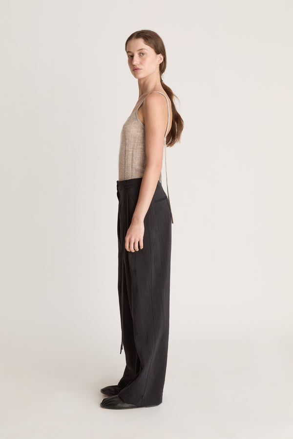 Woman wearing a beige tank top and black pants on a white background