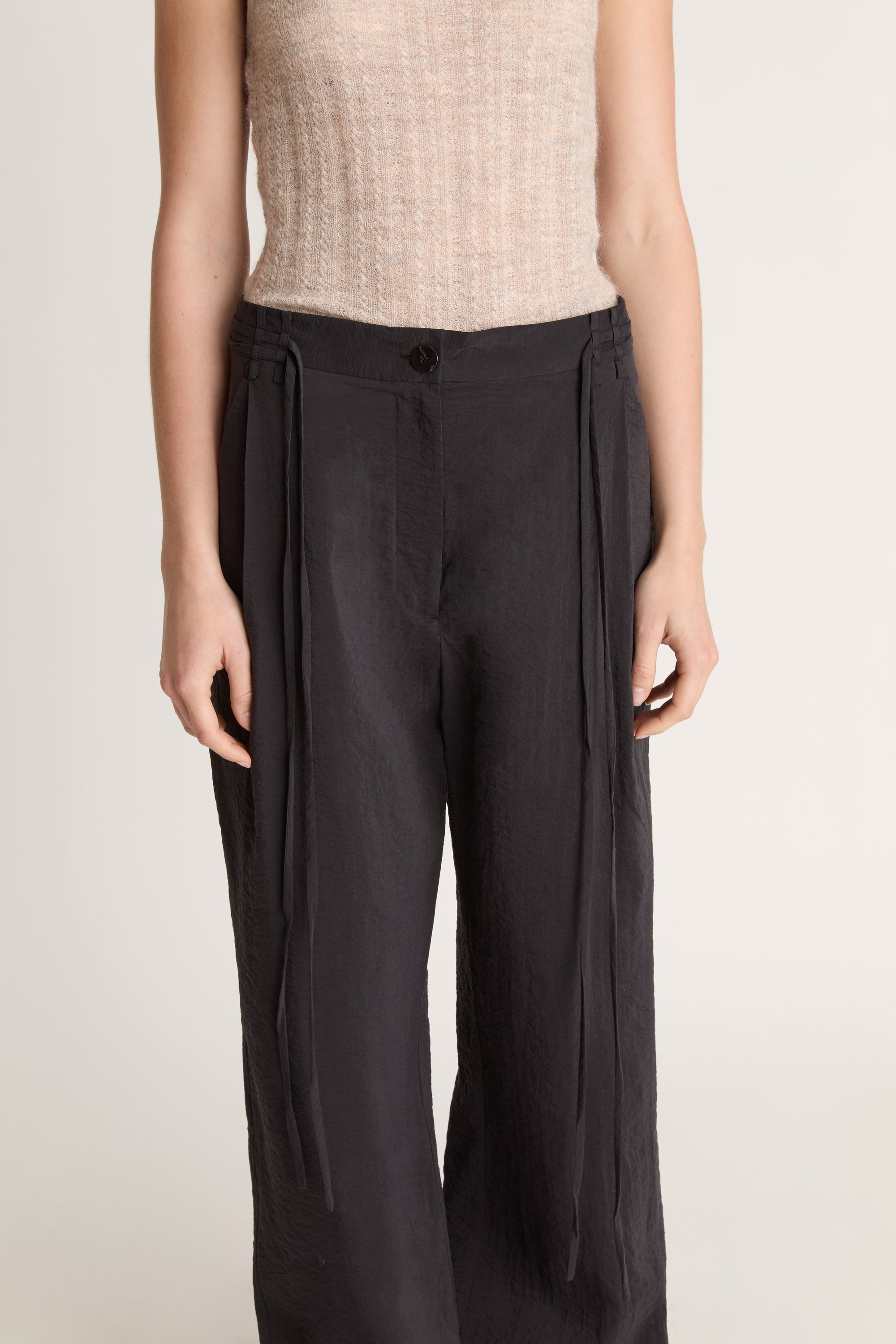 Woman wearing a beige tank top and black pants on a white background