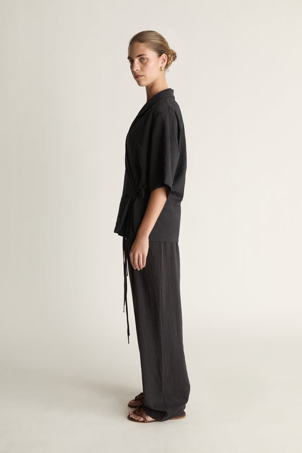 Person wearing a black wrap top with black trousers on a plain background