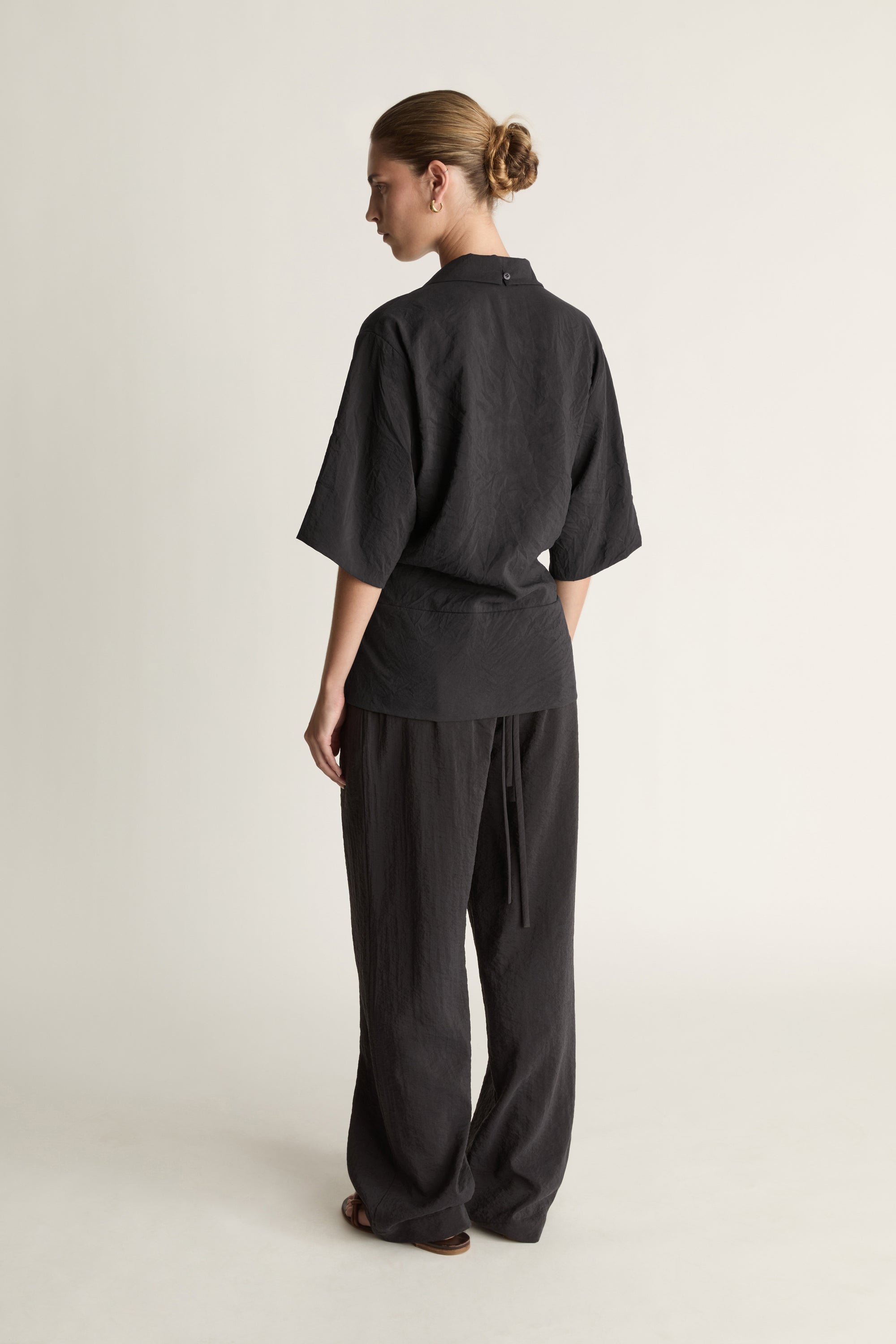 Person wearing a black wrap top with black trousers on a plain background