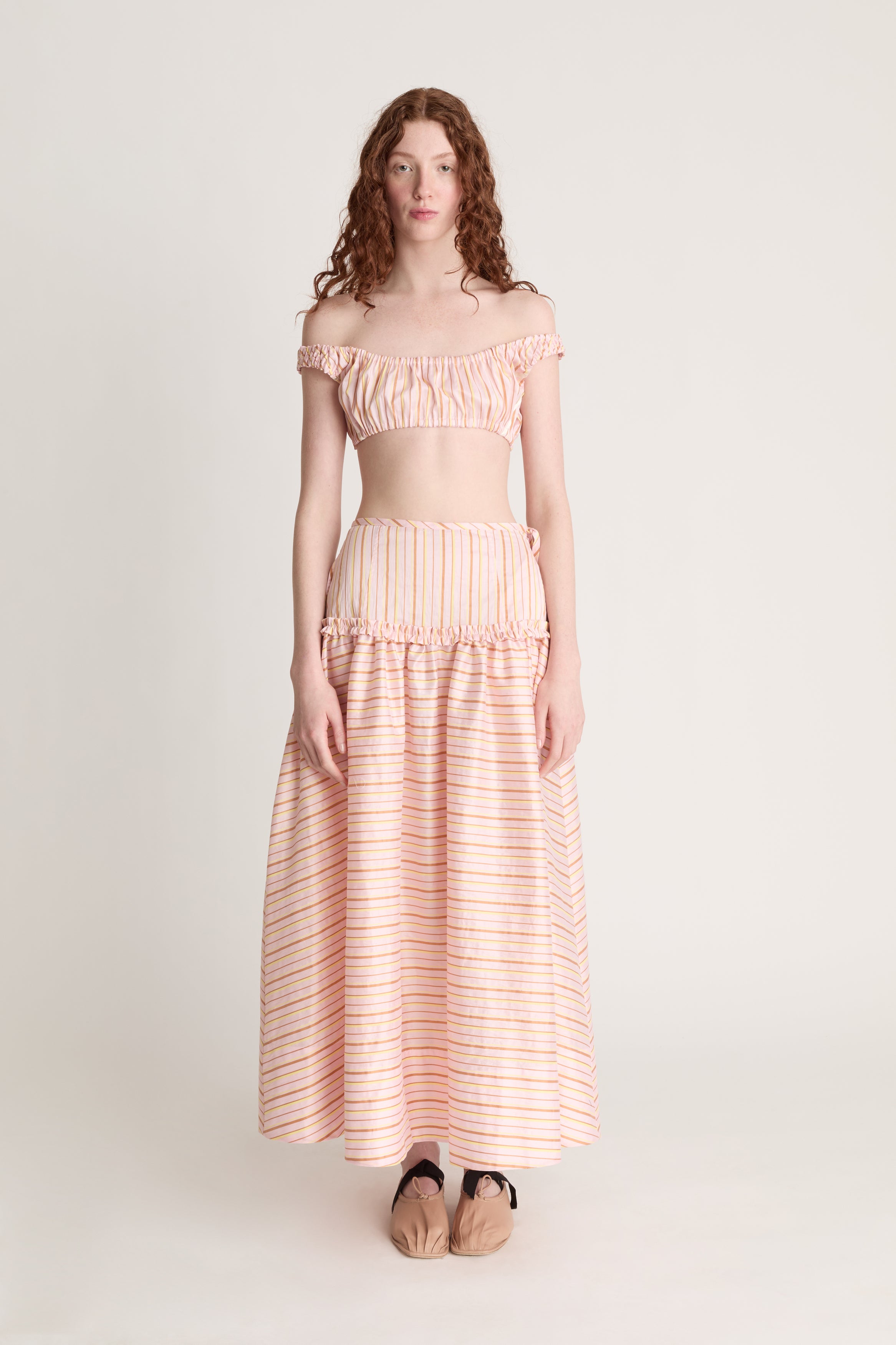 Woman wearing a pink striped crop top and skirt on a plain background