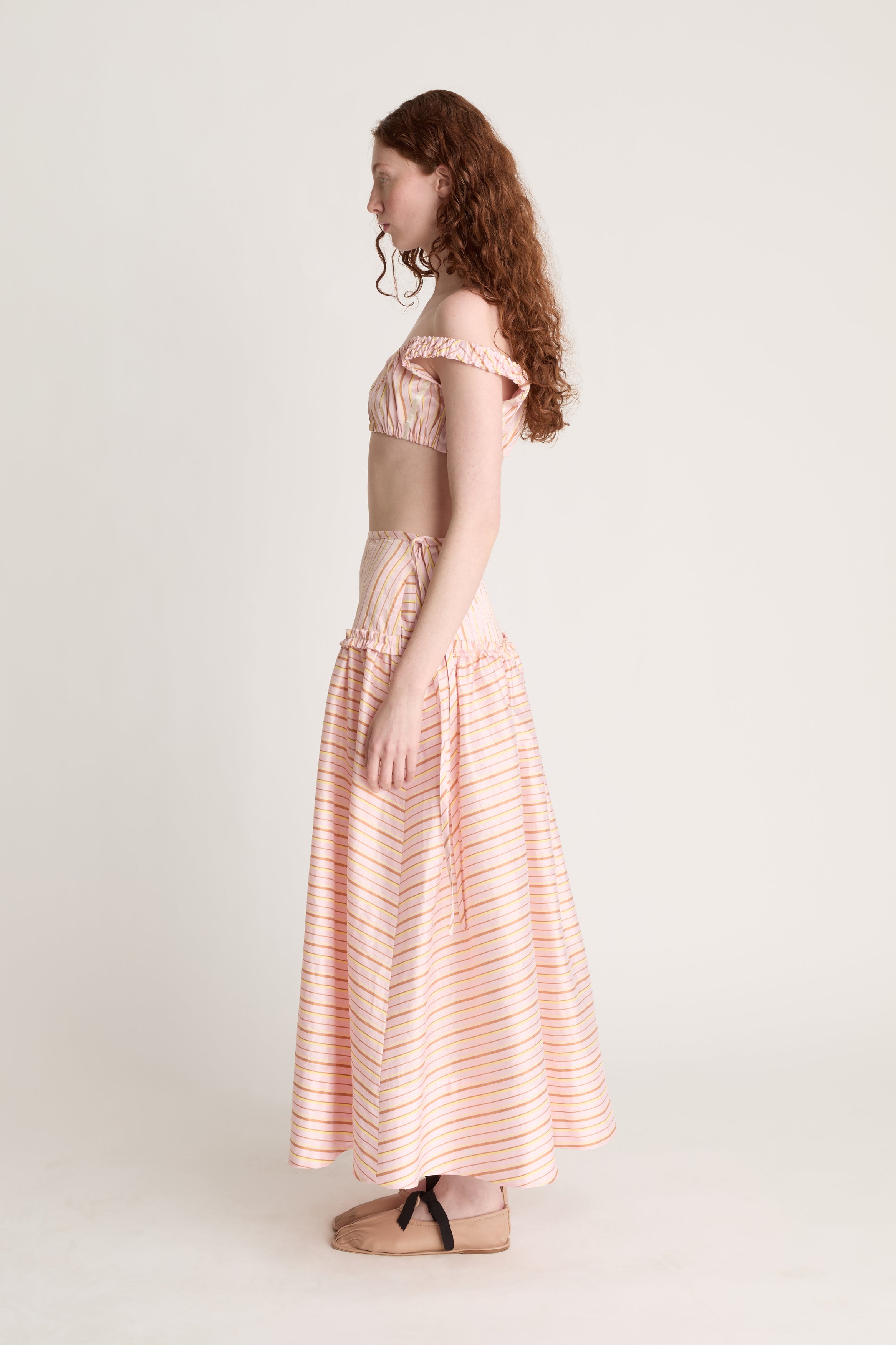 Woman wearing a pink striped crop top and skirt on a plain background