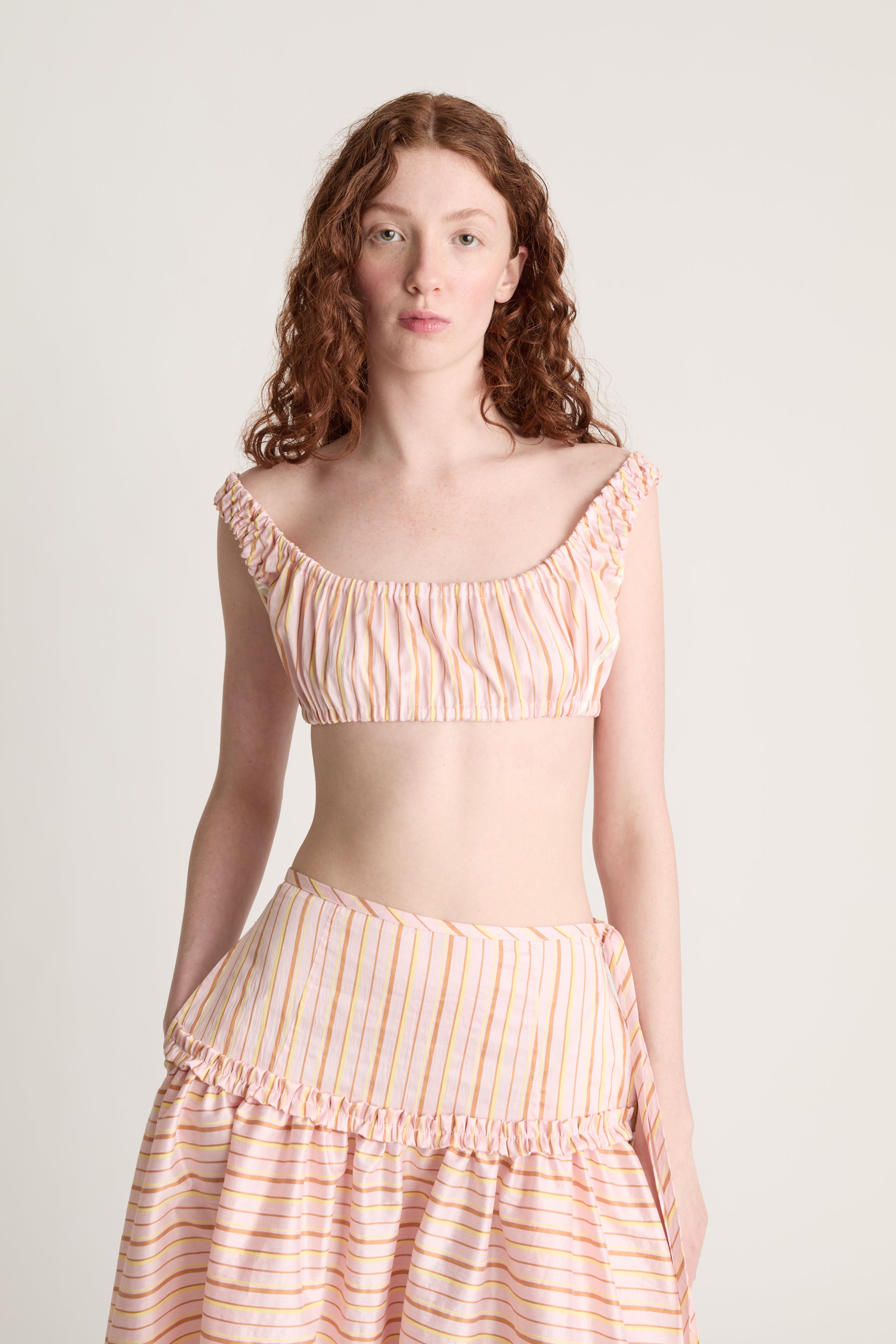 Woman wearing a pink striped crop top and skirt on a plain background