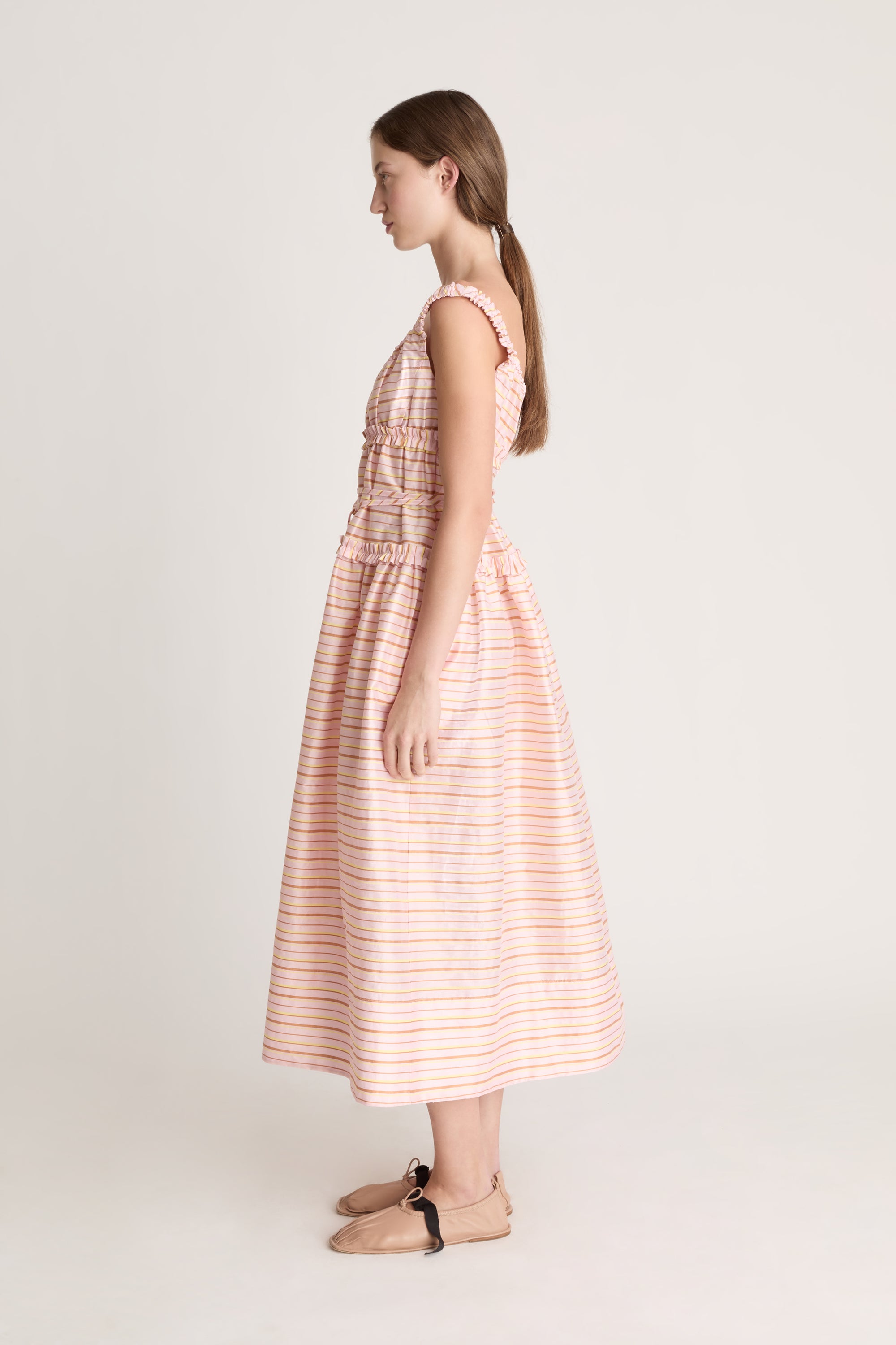 Woman wearing a sleeveless dress with a striped pattern on a plain background