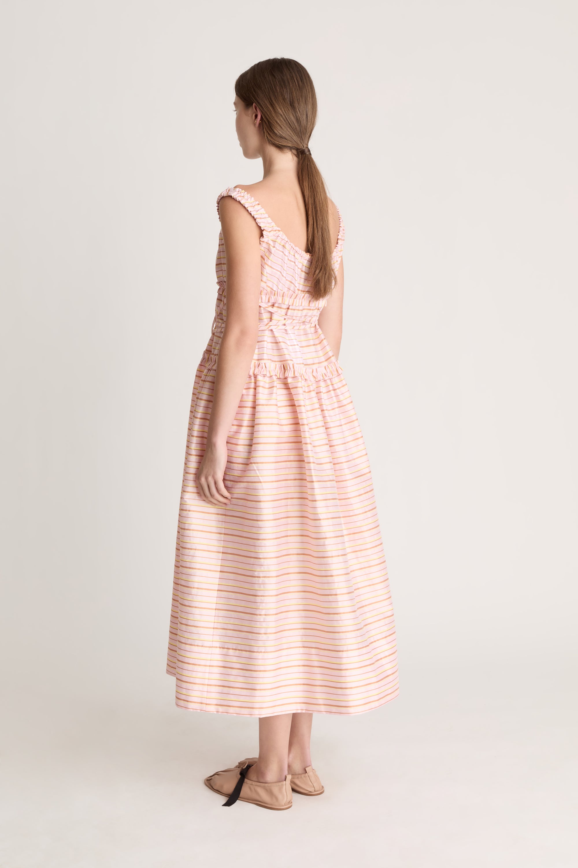 Woman wearing a sleeveless dress with a striped pattern on a plain background