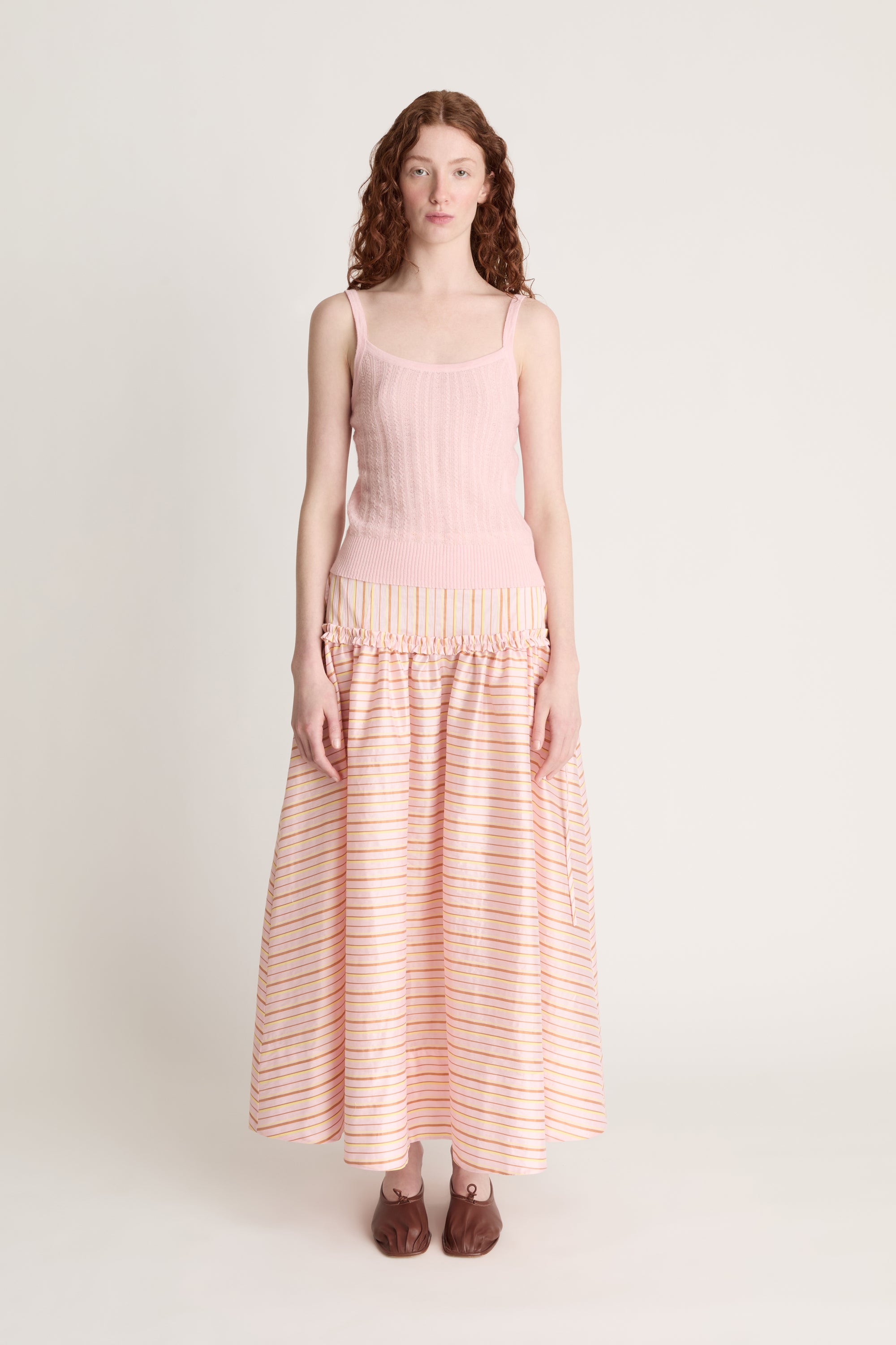 Woman wearing a pink knit cami and a pink striped skirt on a white background