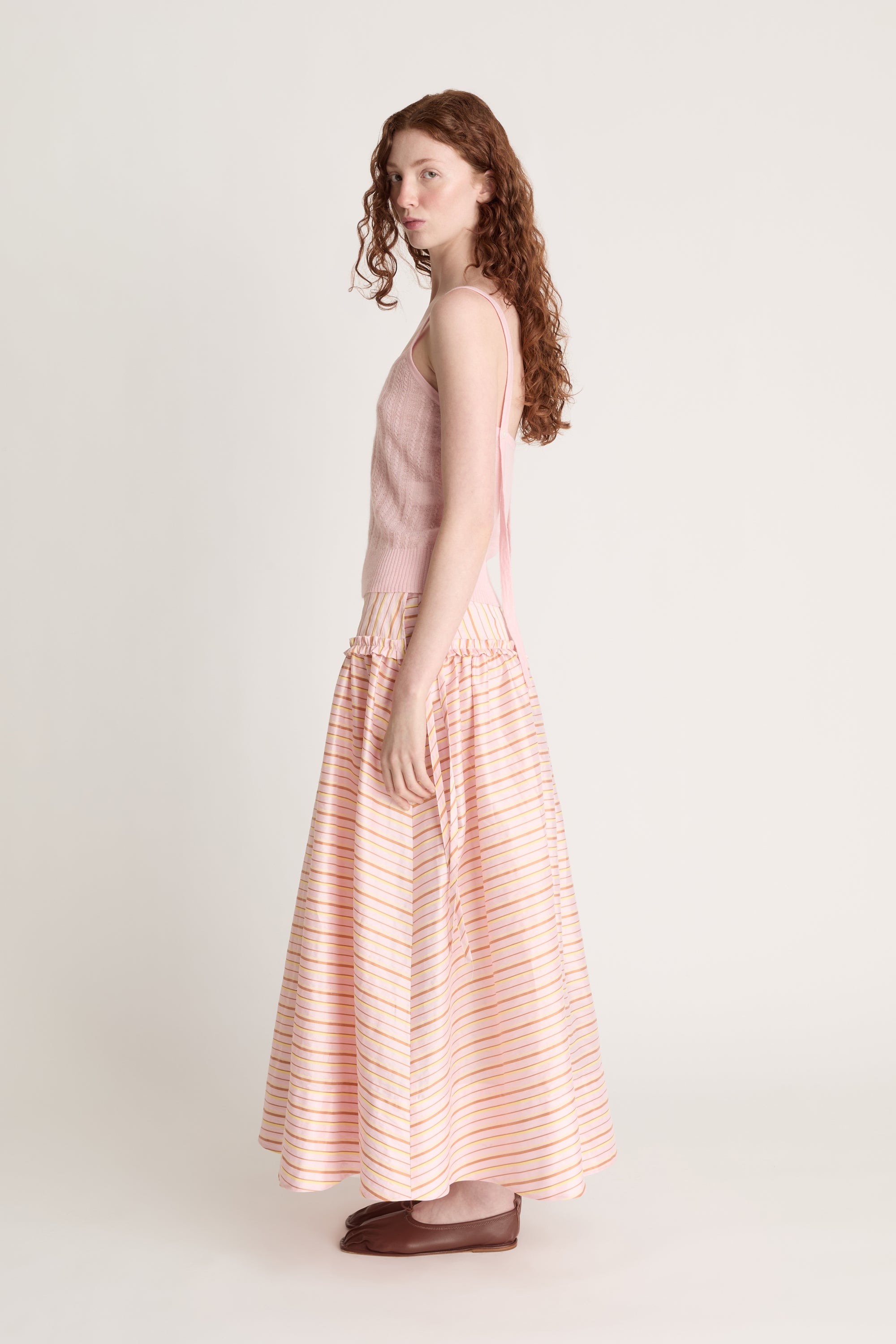 Woman wearing a pink knit cami and a pink striped skirt on a white background