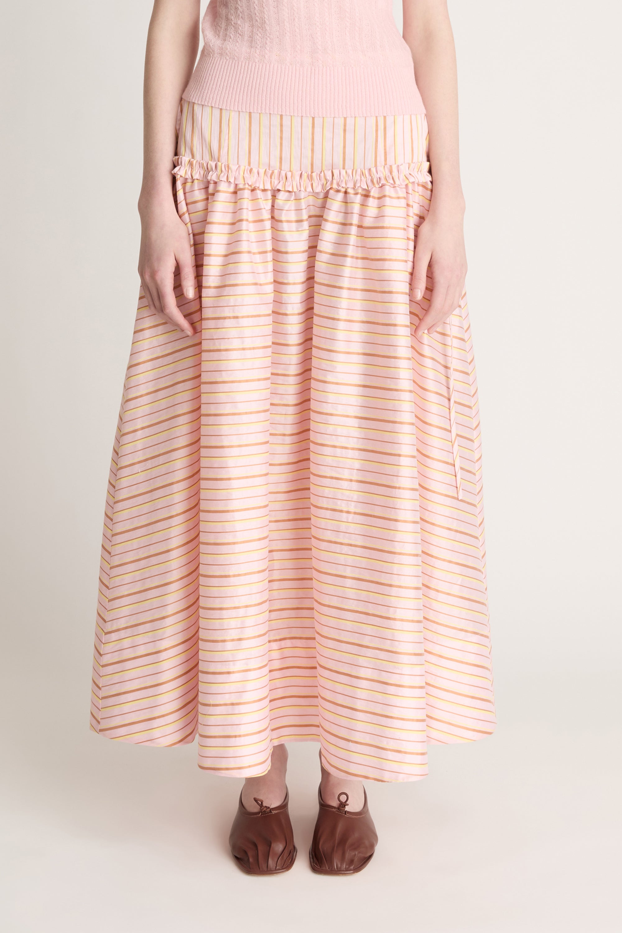 Woman wearing a pink knit cami and a pink striped skirt on a white background