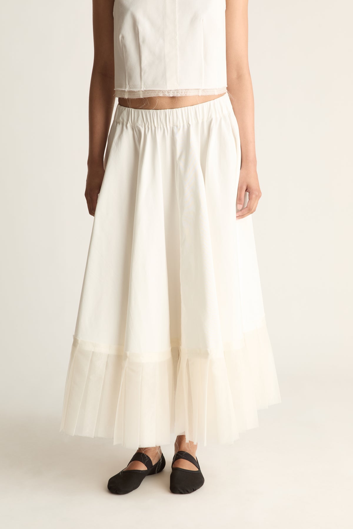 Close-up front view of a cream skirt with an elasticated waist, flared shape and sheer layered hem.